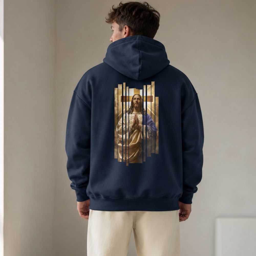 A man viewed from behind wearing a navy blue hoodie with a large graphic print of Jesus Christ on the back, paired with cream-colored pants, in a neutral indoor setting.