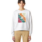 A model wearing a white crewneck sweatshirt with a colorful text graphic that reads 'I AM NOT PERFECT BUT I AM LIMITED EDITION' in a retro block-letter design. The model is also wearing beige pants, set against a plain white studio background.