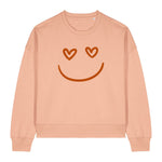 Stanley/Stella Peach-colored sweatshirt with a smiley face design featuring heart eyes on a white background