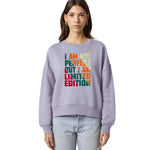 A woman modeling a lavender crewneck sweatshirt with a colorful text graphic on the chest that reads 'I AM NOT PERFECT BUT I AM LIMITED EDITION' in rainbow colors, paired with light-wash jeans against a plain white background.