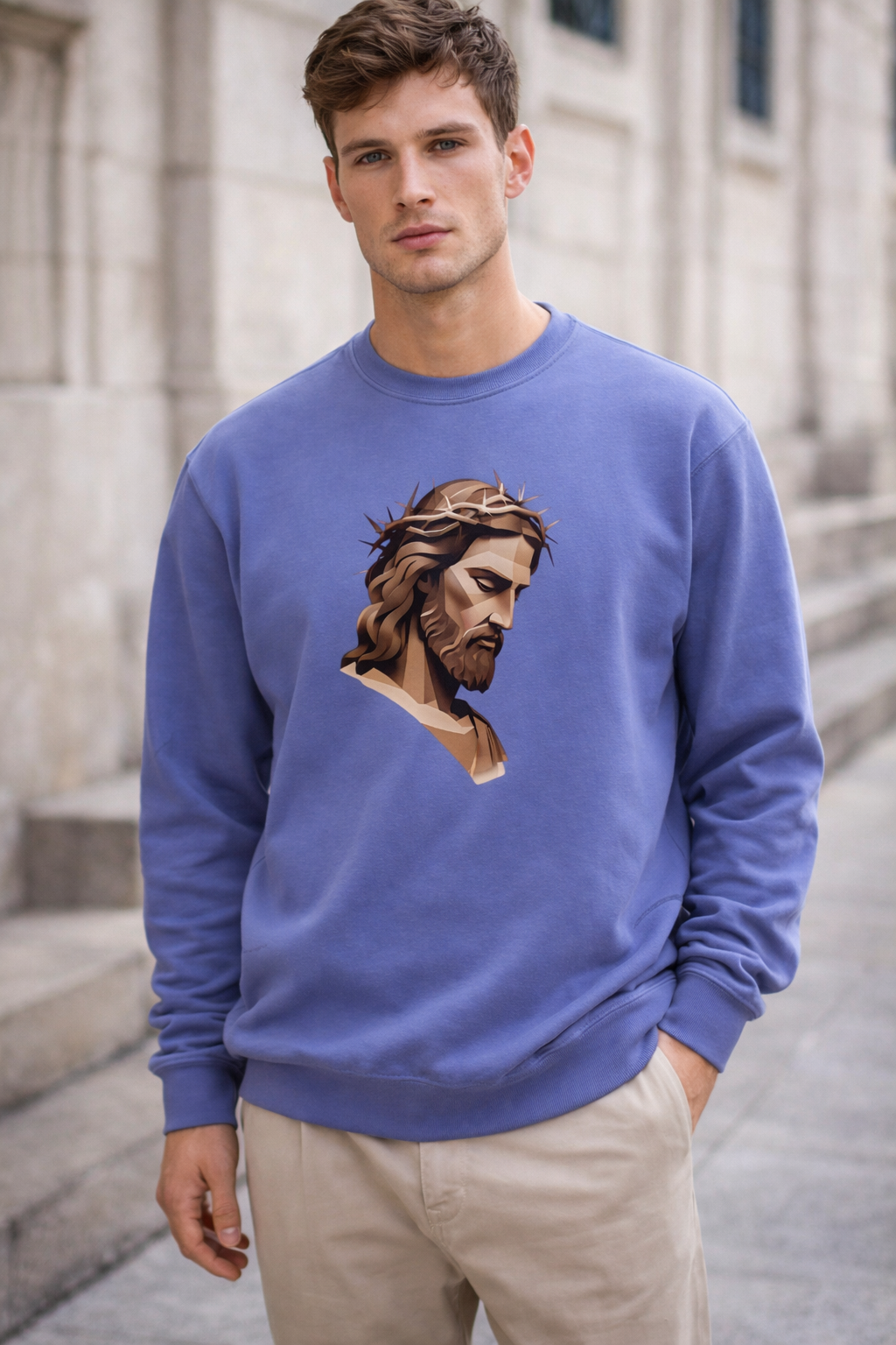 A young man stands outside wearing a light purple sweatshirt featuring an illustrated image of Jesus with a crown of thorns. Stone steps and a building with windows are visible in the background.