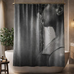 Black and white shower curtain featuring a close-up image of a couple standing under running water, with water streaming down their face and neck. The bathroom includes a bathtub, potted plant, and warm-toned decor.