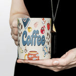 A woman in a black outfit holds a large mug decorated with colorful coffee cups, coffee beans, and the word "Coffee" in bold blue letters.
