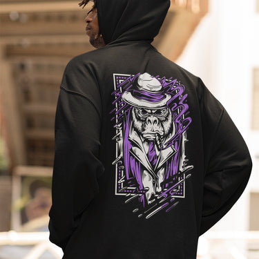 Person wearing a black hoodie with a graphic design of a monkey in a suit and hat on the back.