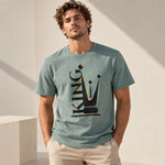 A man wearing a sage green graphic t-shirt with a black and gold crown design that spells 'KING'.