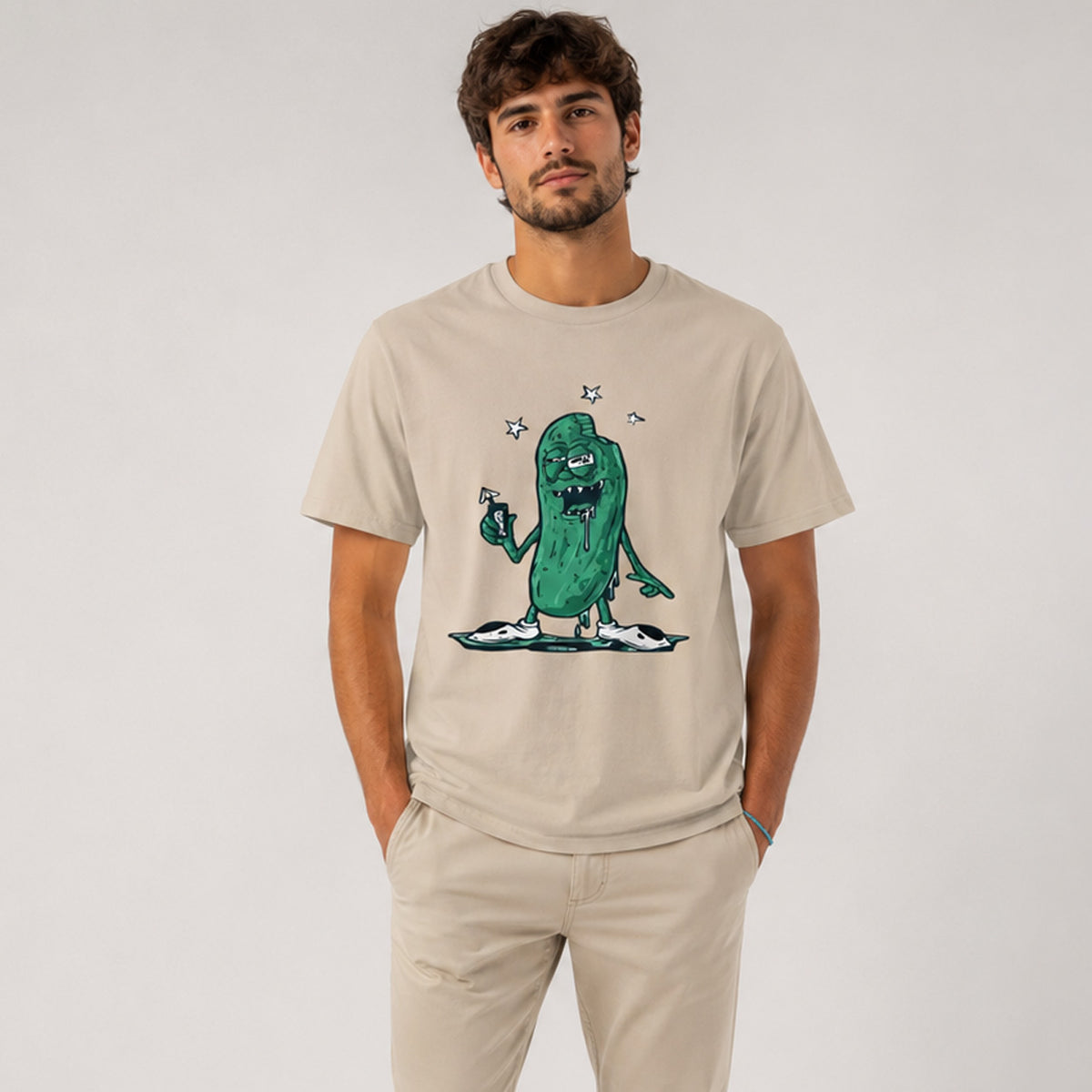 Man wearing a beige t-shirt with a green cartoon character design on a plain background