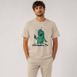 Man wearing a beige t-shirt with a green cartoon character design on a plain background