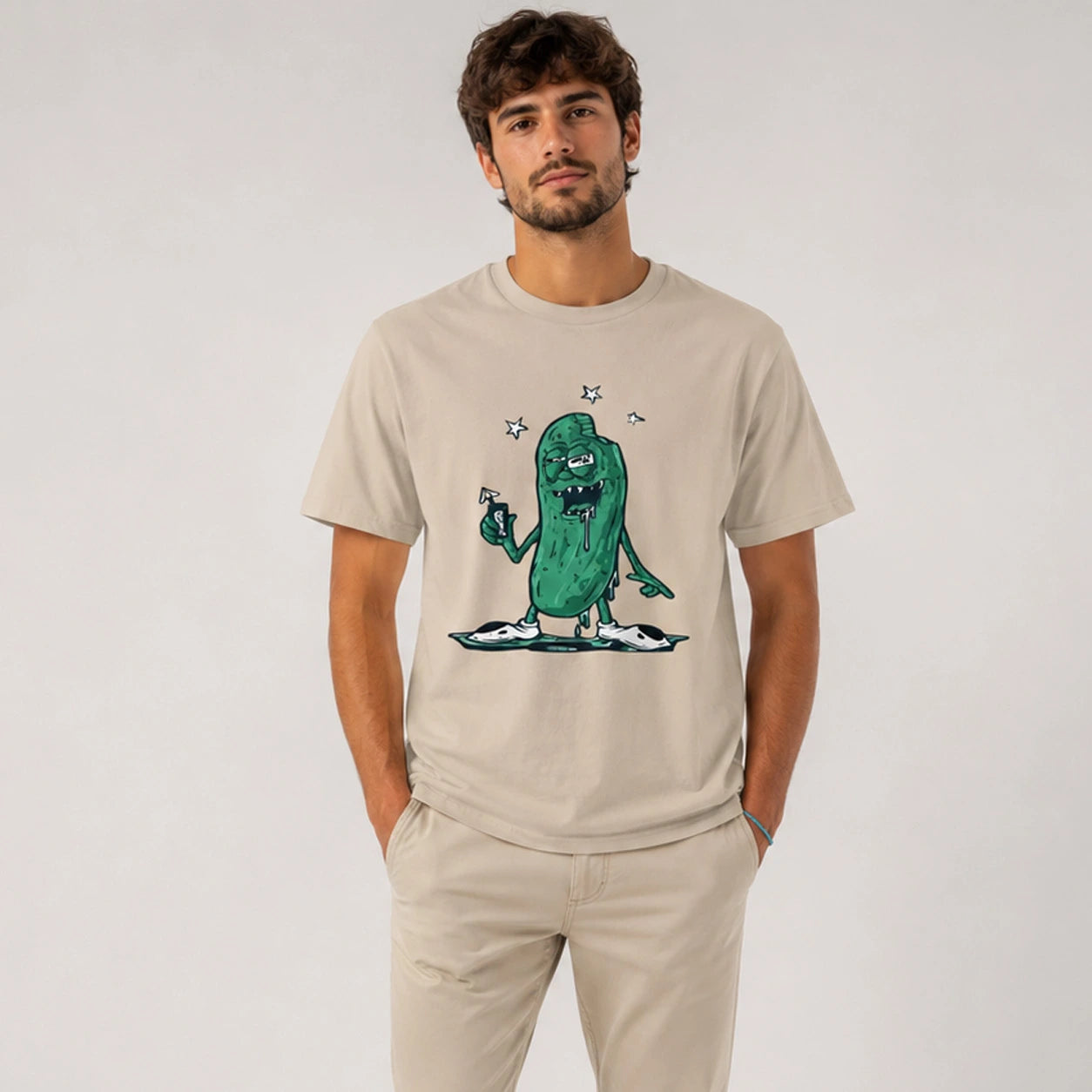 Man wearing a beige t-shirt with a green cartoon character design on a plain background