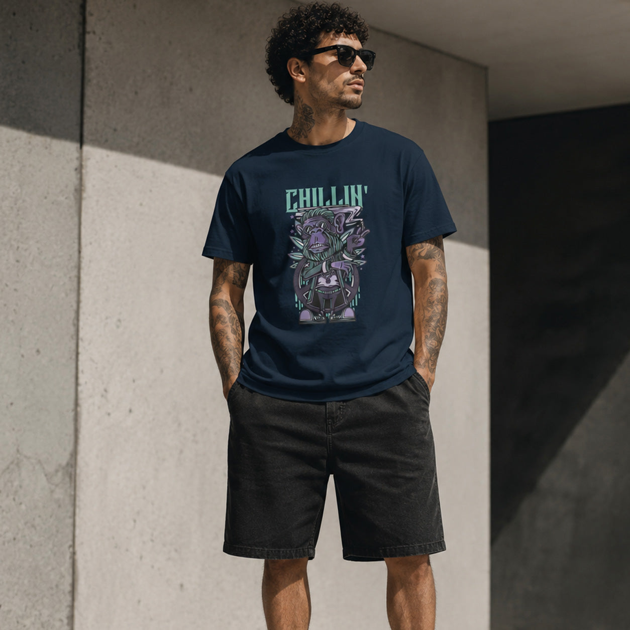 Man wearing a navy blue t-shirt with a graphic design and text, standing against a concrete wall.