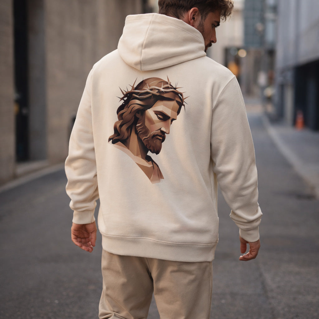 A man wearing a cream-colored hoodie with an artistic image of Jesus wearing a crown of thorns printed on the back, standing in an empty city street.