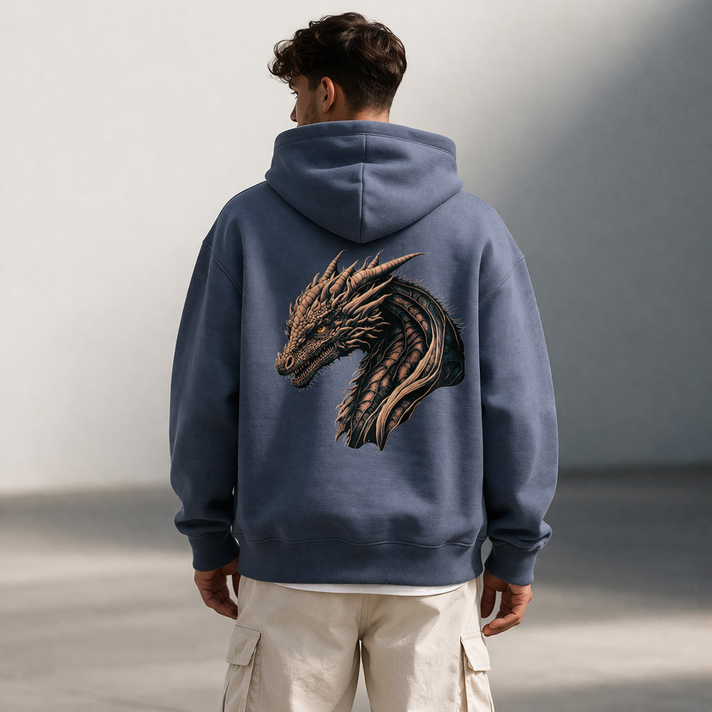 A man wearing a blue hoodie with a detailed dragon head design on the back stands outdoors, facing away from the camera. He also wears light-colored cargo pants.
