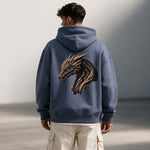 A man wearing a blue hoodie with a detailed dragon head design on the back stands outdoors, facing away from the camera. He also wears light-colored cargo pants.