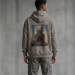 A man stands with his back to the camera, wearing a gray hoodie featuring artwork of a bald figure covering their face. The setting is indoors with a neutral gray background.