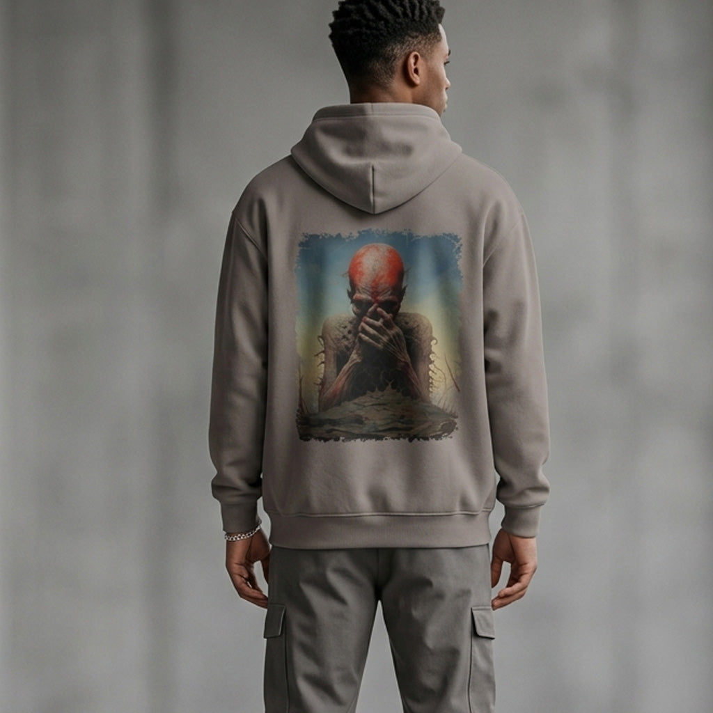 A man stands with his back to the camera, wearing a gray hoodie featuring artwork of a bald figure covering their face. The setting is indoors with a neutral gray background.