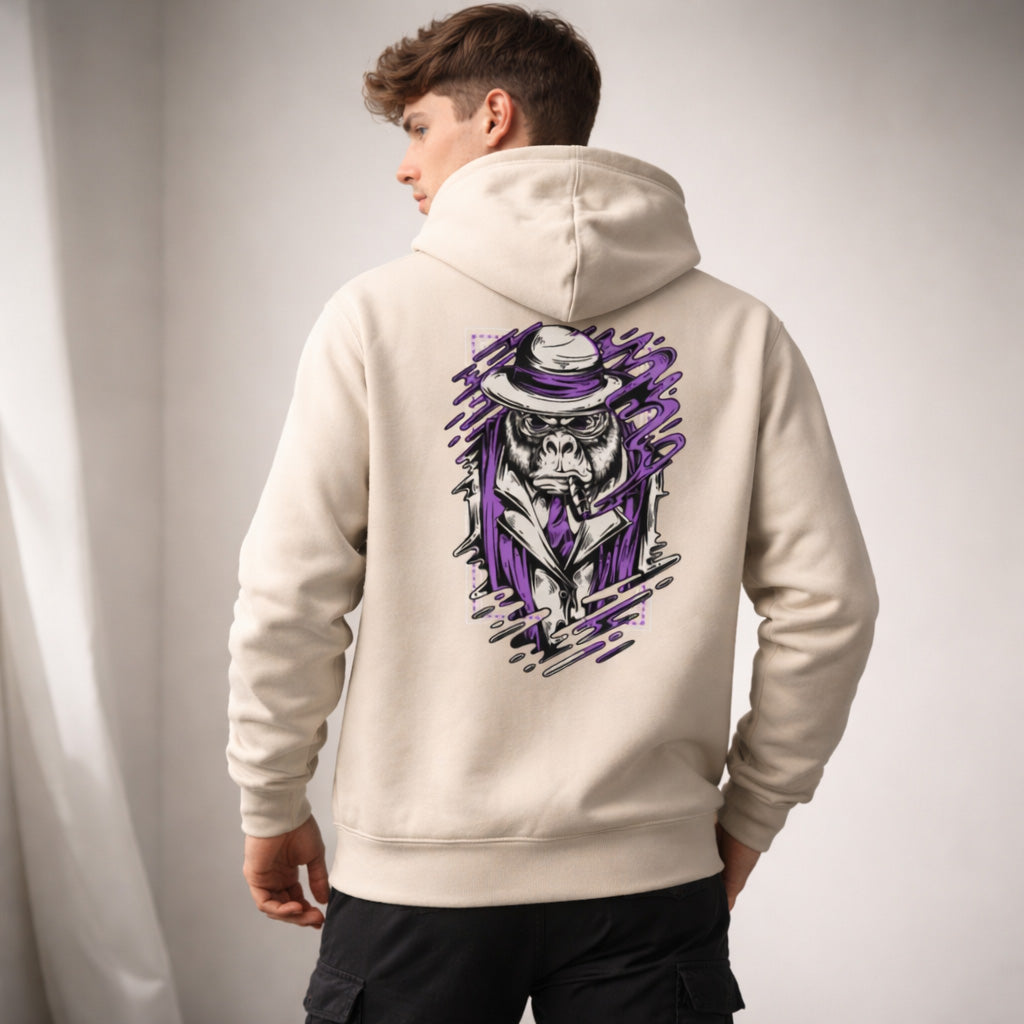 A young man stands with his back to the camera, wearing a light hoodie featuring a graphic of a skull in a purple suit and hat on the back. The background is softly lit with neutral tones.