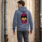 A person wearing a gray hoodie with a graphic of a wolf in a purple hat on the back stands in an alleyway, facing away from the camera. The alley has a brick wall and metal pipes.