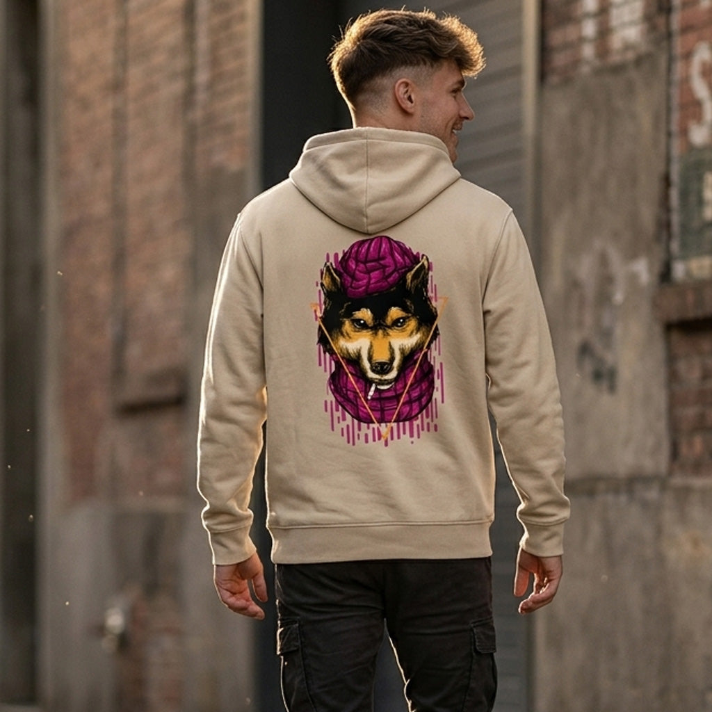 A man stands outdoors wearing a tan hoodie with a colorful graphic of a dog in a purple hood on the back. He faces away from the camera, walking along a brick and concrete building.