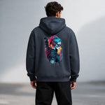 A man wearing a dark hoodie with a colorful graphic on the back depicting a futuristic, masked character with bright hair and cyberpunk elements. The man is standing outdoors, facing away from the camera.