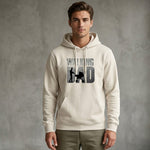 A man wearing a light-colored hoodie with the words "WALKING DAD" and an image of a man pushing a stroller printed on the front stands against a plain gray background.
