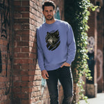 Man wearing a blue sweatshirt with a wolf design, leaning against a brick wall.
