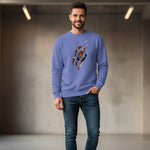 A man with short brown hair and a beard wears a lavender sweatshirt with an abstract  tiger design and blue jeans, standing in a modern indoor setting with grey walls and ceiling lights.