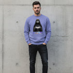 A man stands against a concrete wall, wearing a lavender sweatshirt featuring an illustrated nun in black robes and the word "FAITH" in bold letters beneath the image. He has dark hair and a trimmed beard.