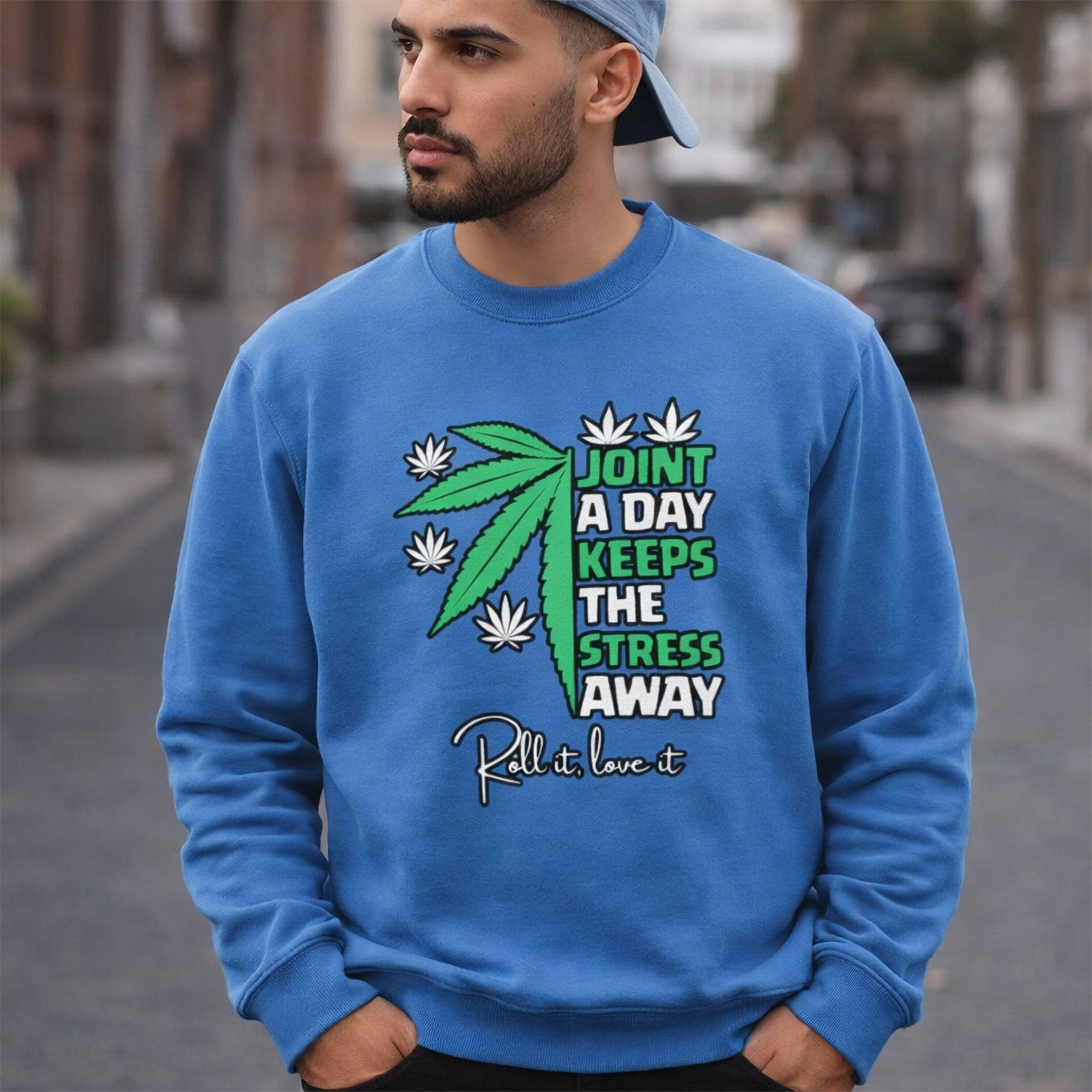 A man wearing a blue cap and blue sweatshirt with a graphic of a cannabis leaf and text: "Joint a day keeps the stress away. Roll it, love it," stands on a city street.