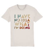 A light beige womens crewneck t-shirt featuring a retro-style typographic graphic that reads 'I HAVE NO IDEA WHAT I'M DOING' in stacked, distressed letters of varying colors including teal, tan, brown, and red.