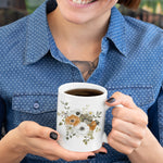 Person holding a white mug with floral design, wearing a blue polka dot shirt.