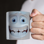 A person holding a white mug with a cartoonish, exaggerated smiling face printed on it, featuring large blue eyes and big teeth.