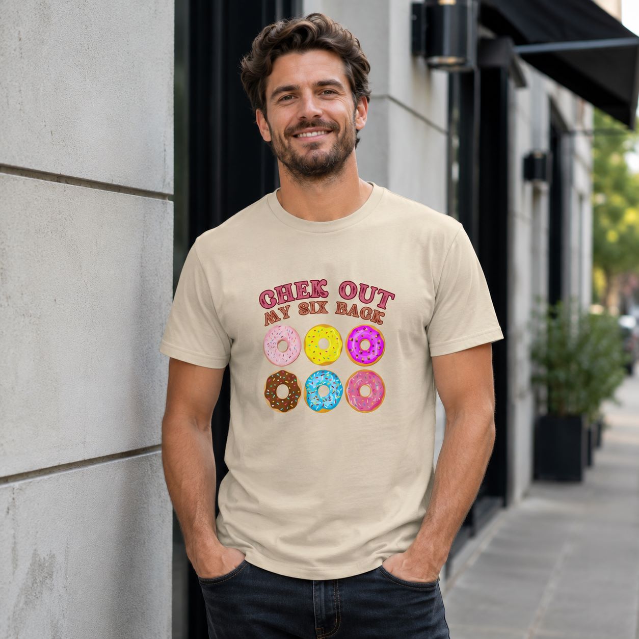 Man wearing a beige t-shirt with colorful donut graphics and text on a city street.