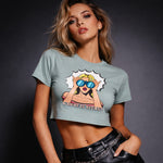 A woman poses against a dark background wearing a cropped light blue t-shirt with a pop art graphic of a blonde woman in sunglasses and the text “WHERE IS YOURS?” She also wears black leather pants with a chain belt.
