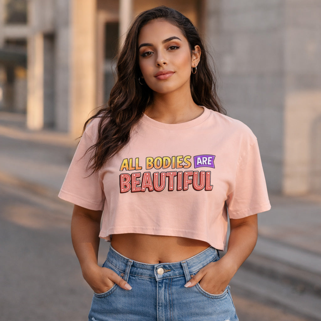 Woman wearing a pink t-shirt with 'All Bodies Are Beautiful' text, standing outdoors.