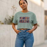 Woman wearing a green crop t-shirt with 'JESUS SAVES' text and blue jeans outdoors.