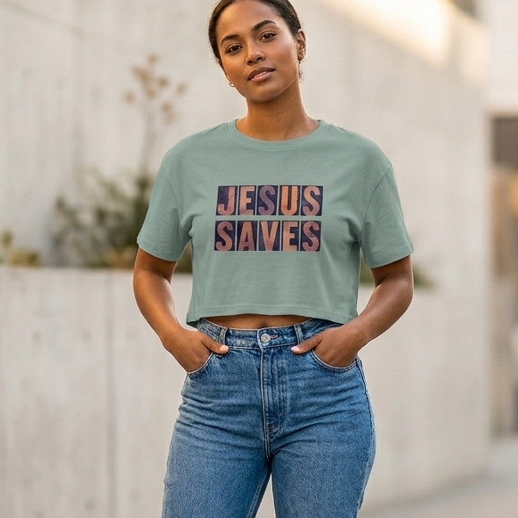 Woman wearing a green crop t-shirt with 'JESUS SAVES' text and blue jeans outdoors.