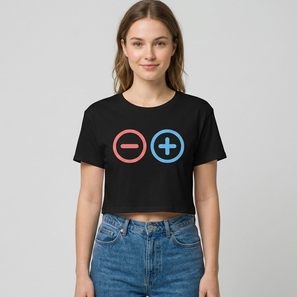 A woman wearing a black crop top with a red minus sign in a circle and a blue plus sign in a circle, standing against a plain, light-colored background.