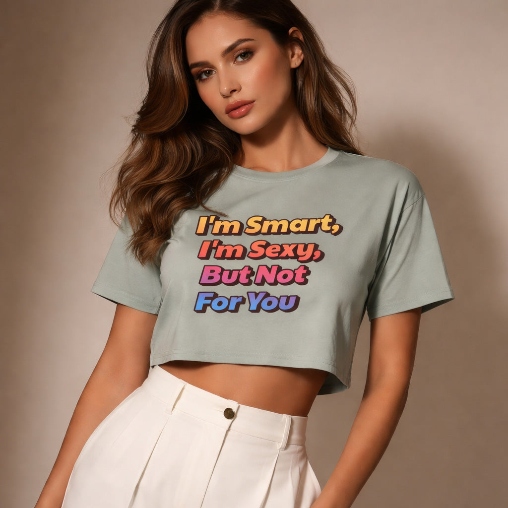 A woman with long brown hair wearing a light gray crop top with colorful text that reads, "I'm Smart, I'm Sexy, But Not For You," paired with high-waisted white pants, stands against a neutral background.