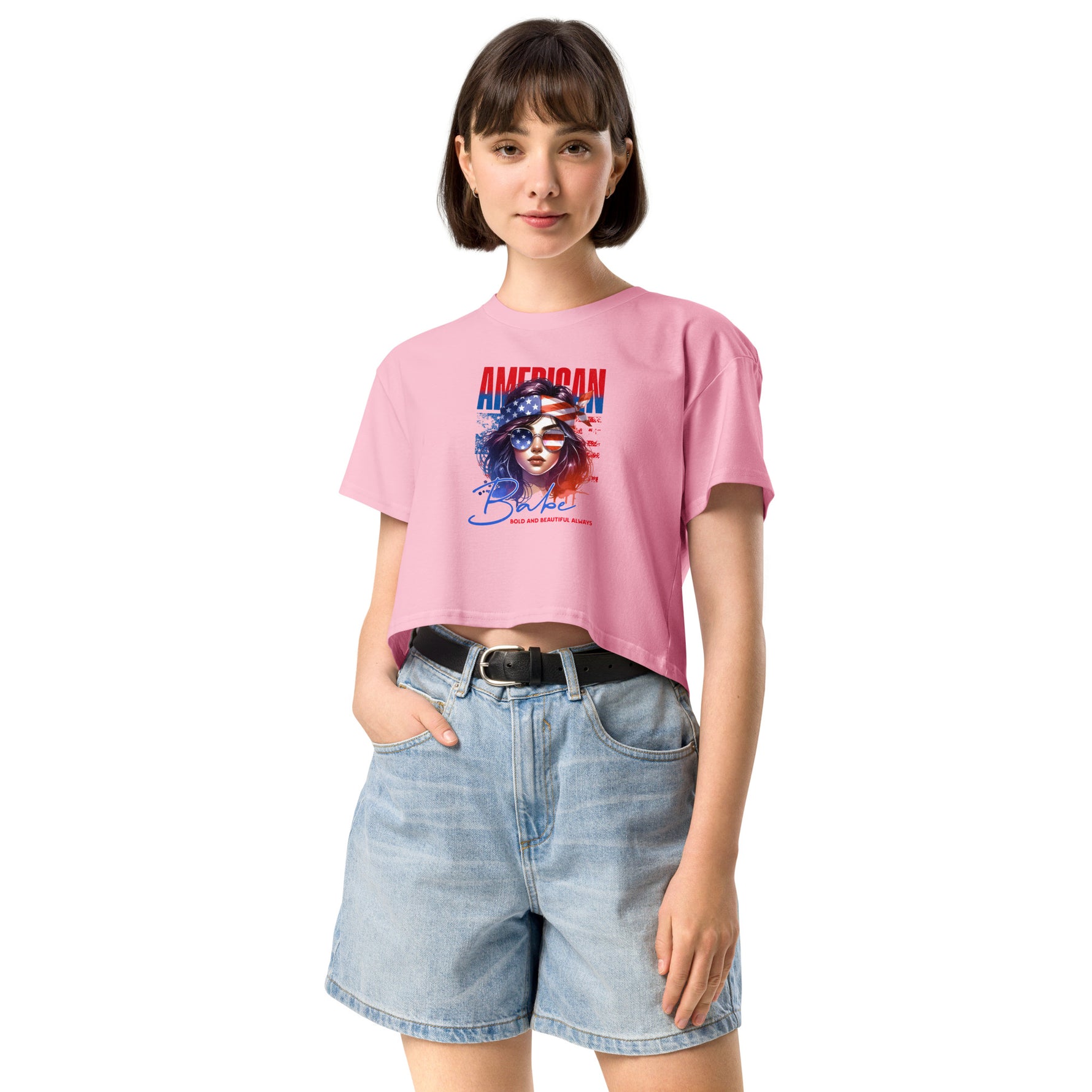 Woman wearing a pink crop t-shirt with a graphic design and denim shorts on a white background