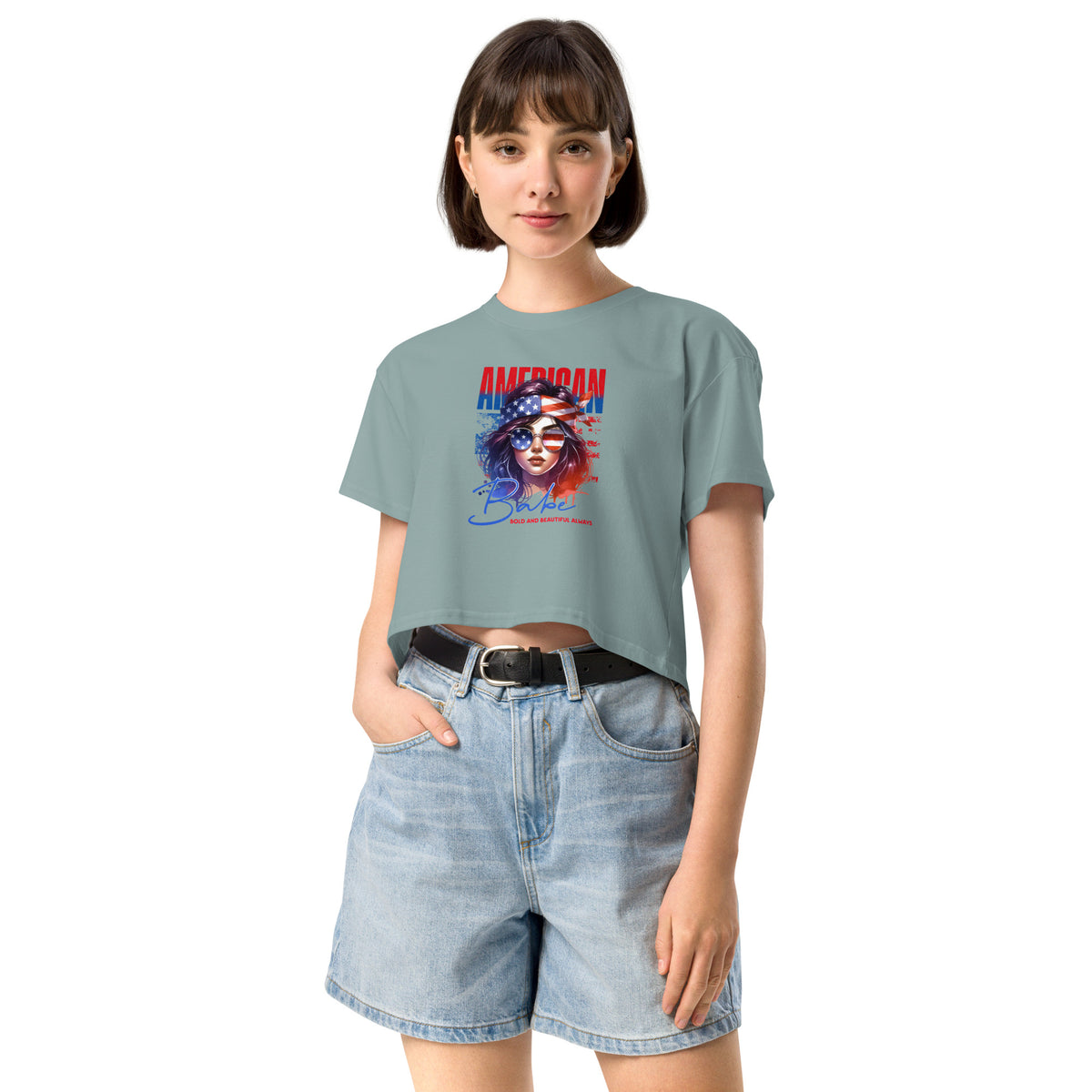 Woman wearing a light blue crop t-shirt with a graphic design and denim shorts on a white background