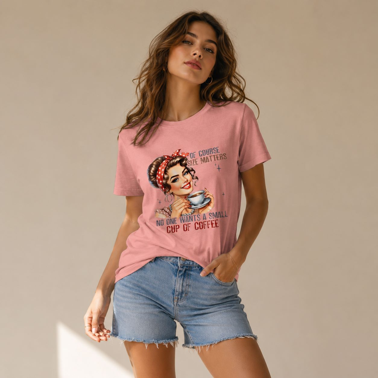 A woman modeling a pink graphic t-shirt with a retro-style pin-up illustration and the text 'YOU ARE IMPORTANT ENOUGH TO DRINK A SMALL CUP OF COFFEE', paired with denim shorts against a neutral beige background.