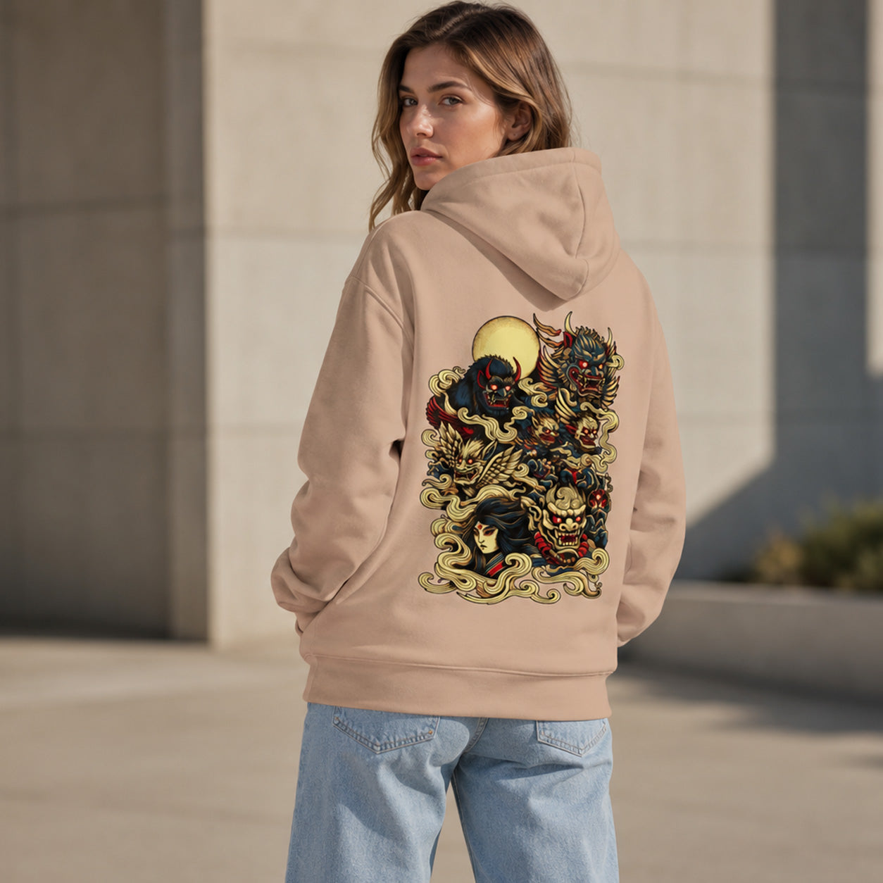 A woman wearing a beige hoodie with a large, detailed multicolor graphic print on the back, shown from behind in an outdoor setting.