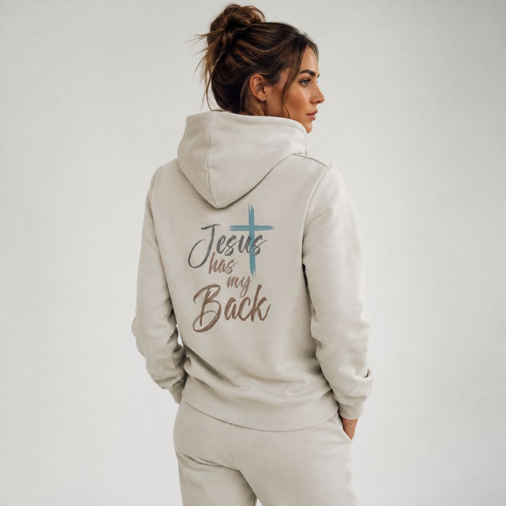 A woman shown from the back wearing a light beige hoodie with the text 'Jesus has my Back' and a blue cross graphic printed on the back, paired with matching beige pants against a plain light gray studio background.