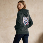 Woman wearing a dark green hoodie with a colorful tiger design on the back against a beige background