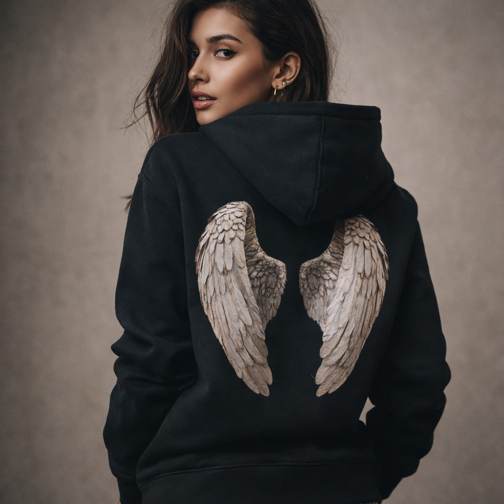 Woman wearing a black hoodie with angel wings design on the back against a neutral background