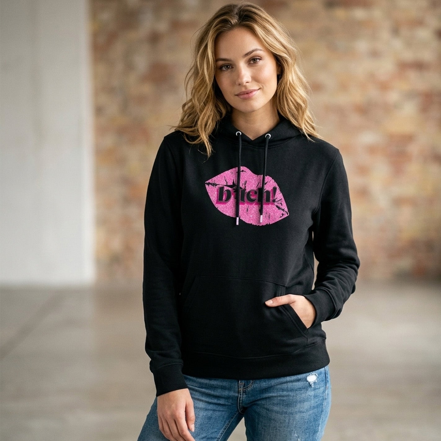 Woman wearing a black hoodie with pink graphic design and text, standing against a neutral background.