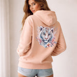 Woman wearing a peach hoodie with a tiger design on the back against a plain background