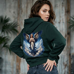 Woman wearing a green hoodie with an angel design on the back, standing against a wooden wall.