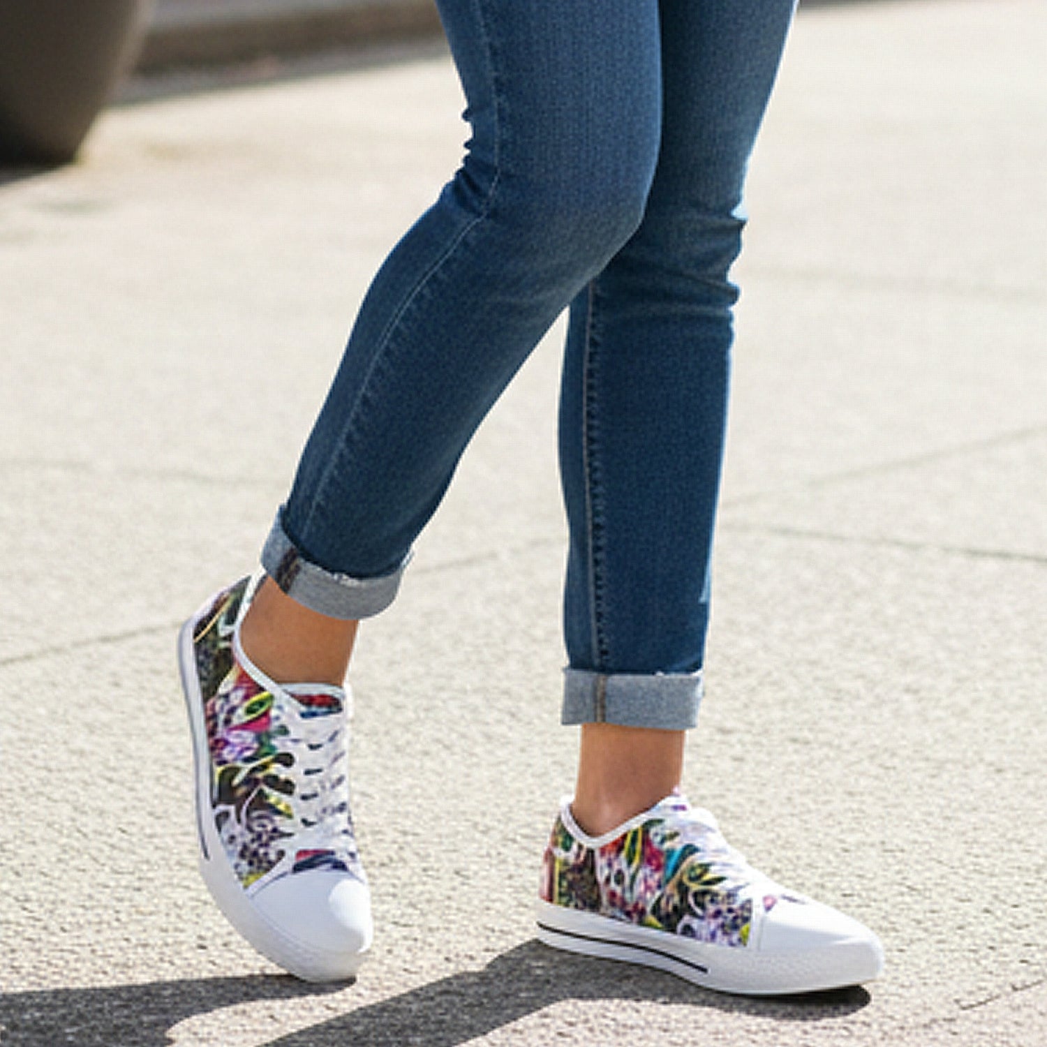 Person wearing graffity pattern sneakers with rolled-up jeans on a pavement.