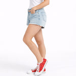 Woman wearing light blue denim shorts and red high-top sneakers on a white background