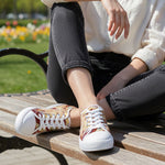 Woman wearing patterned sneakers sitting on a wooden bench with a blurred outdoor background